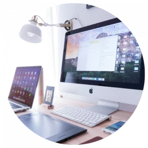 Circular image containing picture of a mac computer on a desk with a white wall light.